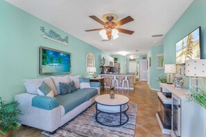 A living room with a sofa, coffee table, and a ceiling fan. - Grand Caribbean 111- ground level by pool (Orange Beach)