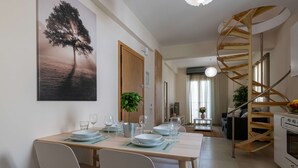 Un comedor con una mesa preparada para cuatro personas, una escalera de caracol y una cocina visible al fondo.