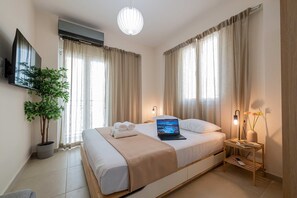 Una habitación de hotel moderna con una cama grande, un televisor de pantalla plana en la pared, una planta en maceta y una mesita de noche con una lámpara y un jarrón con flores.
