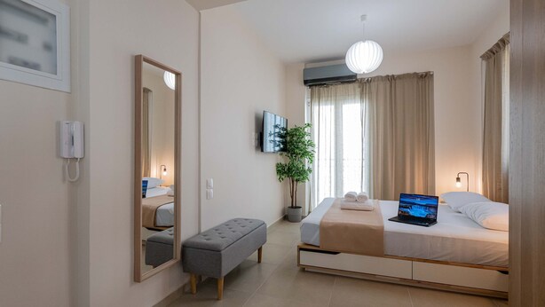 A modern hotel room with a bed, a bench, a potted plant, a TV, and a mirror. - Home Easy Kalamata - Central Nest Private Parking (Kalamata)