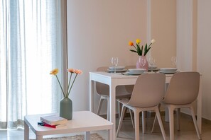 Un coin repas avec une table dressée pour deux personnes, un vase rempli de fleurs et une fenêtre avec des rideaux.