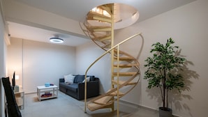 Een moderne woonkamer met een spiltrap, een grijze bank, een klein wit tafeltje en een potplant.