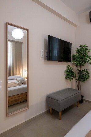 A modern hotel room with a large mirror, a flat-screen TV, a bench, and a potted plant. - Home Easy Kalamata - Central Nest Private Parking (Kalamata)