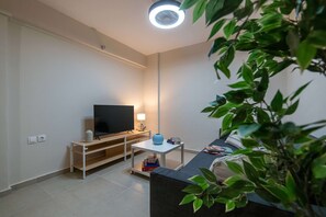 A modern living room with a flat-screen TV, a small table with a lamp, a sofa, and a potted plant. - Home Easy Kalamata - Central Nest Private Parking (Kalamata)