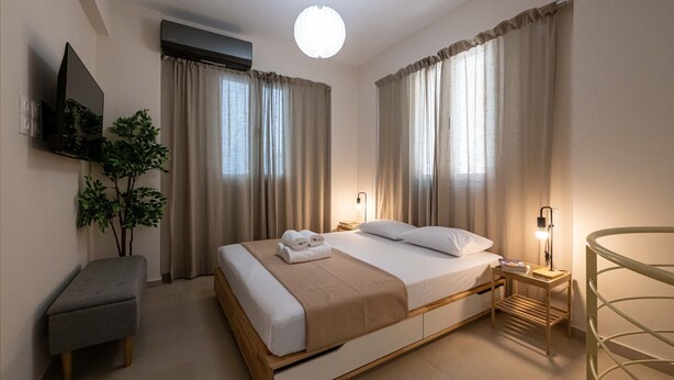Een moderne hotelkamer met een bed, nachtkastje, lamp en een klein krukje.