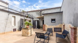 A patio with outdoor furniture, a stone planter, and a brick wall. - La Papuzzella – Spacious Apartment with Terrace and Scenic Views (Mascali)