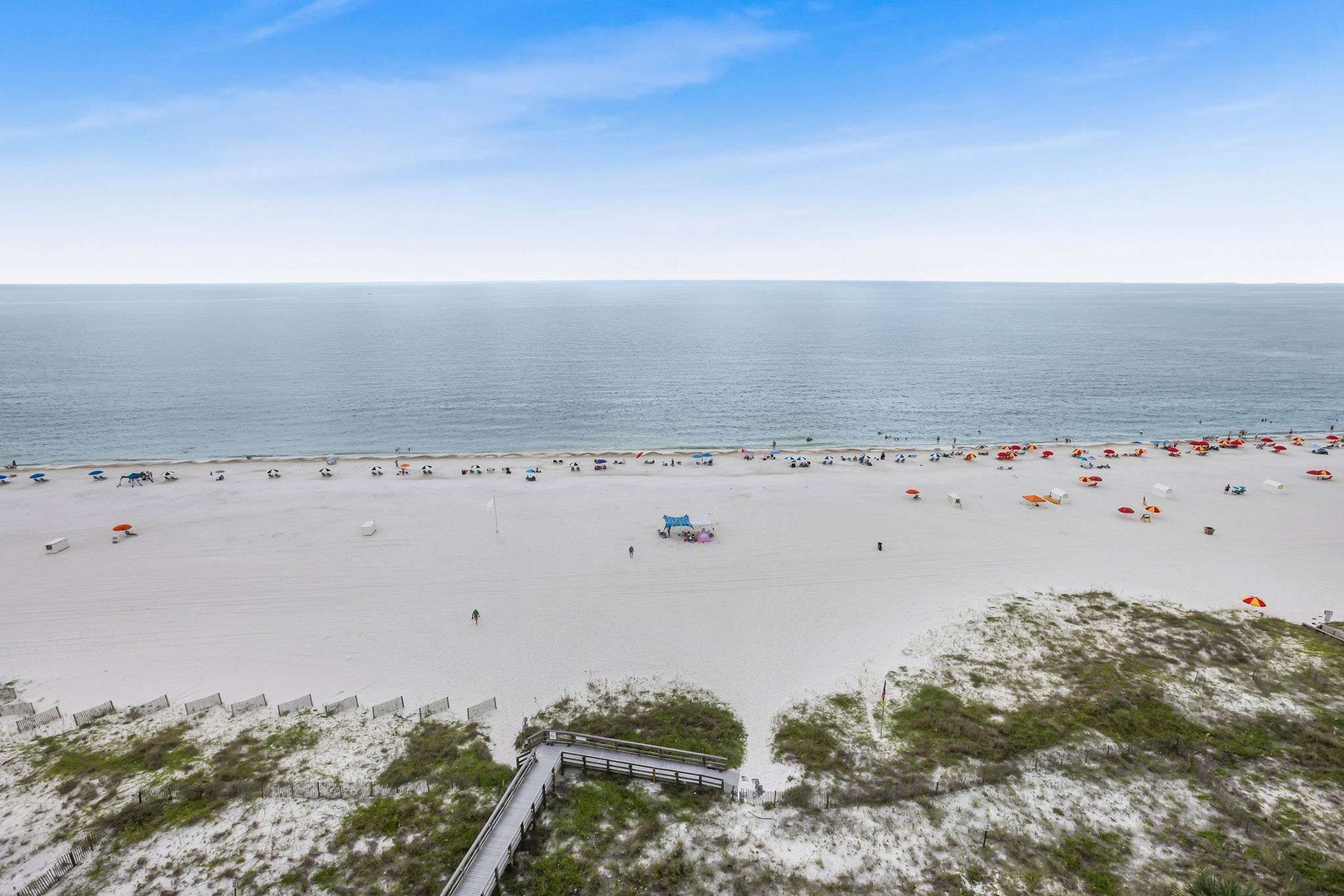 A beach with a wooden walkway leading to a structure, white sand, and a clear sky.