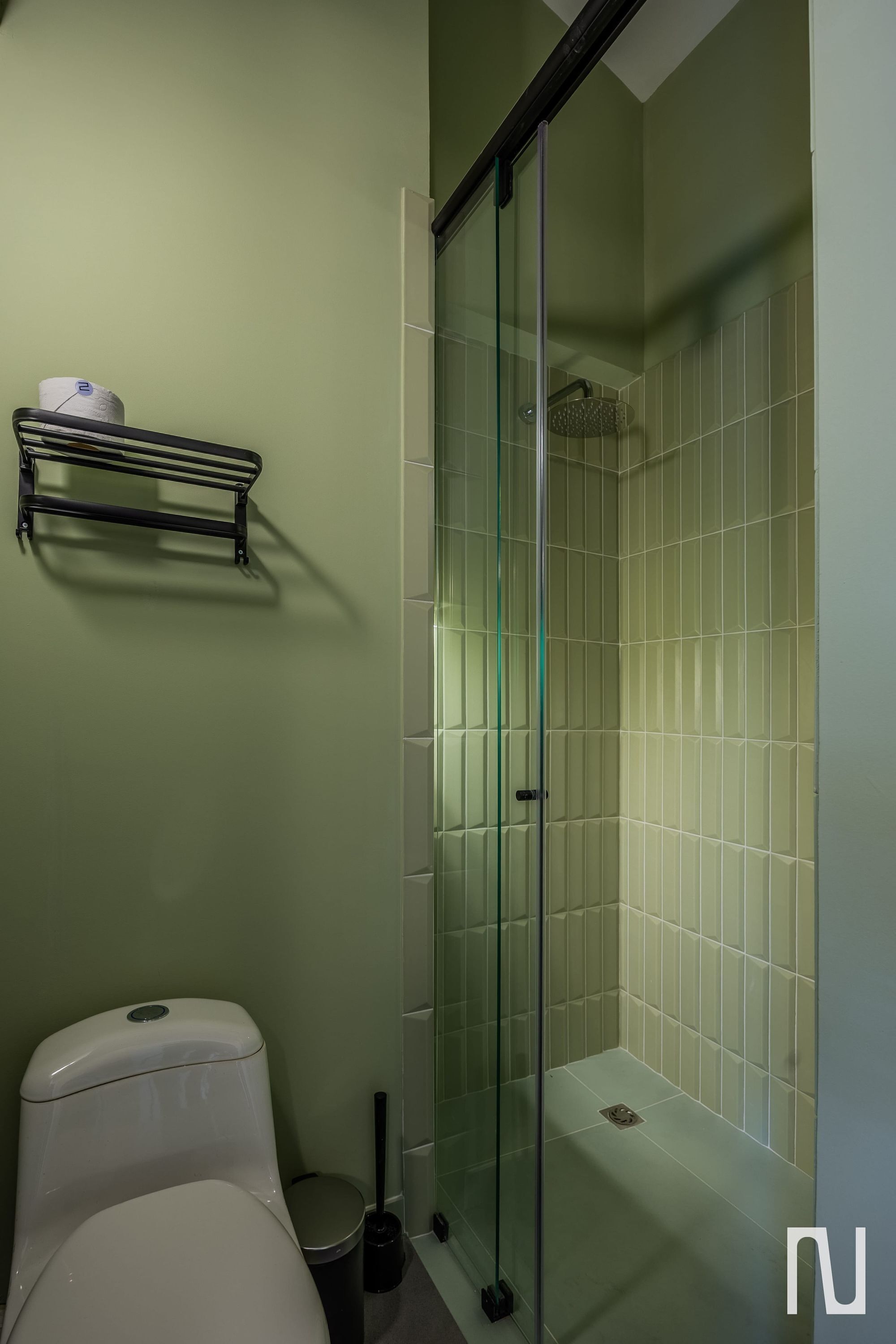 A bathroom with a toilet, a glass-enclosed shower, and a shelf with a roll of toilet paper.