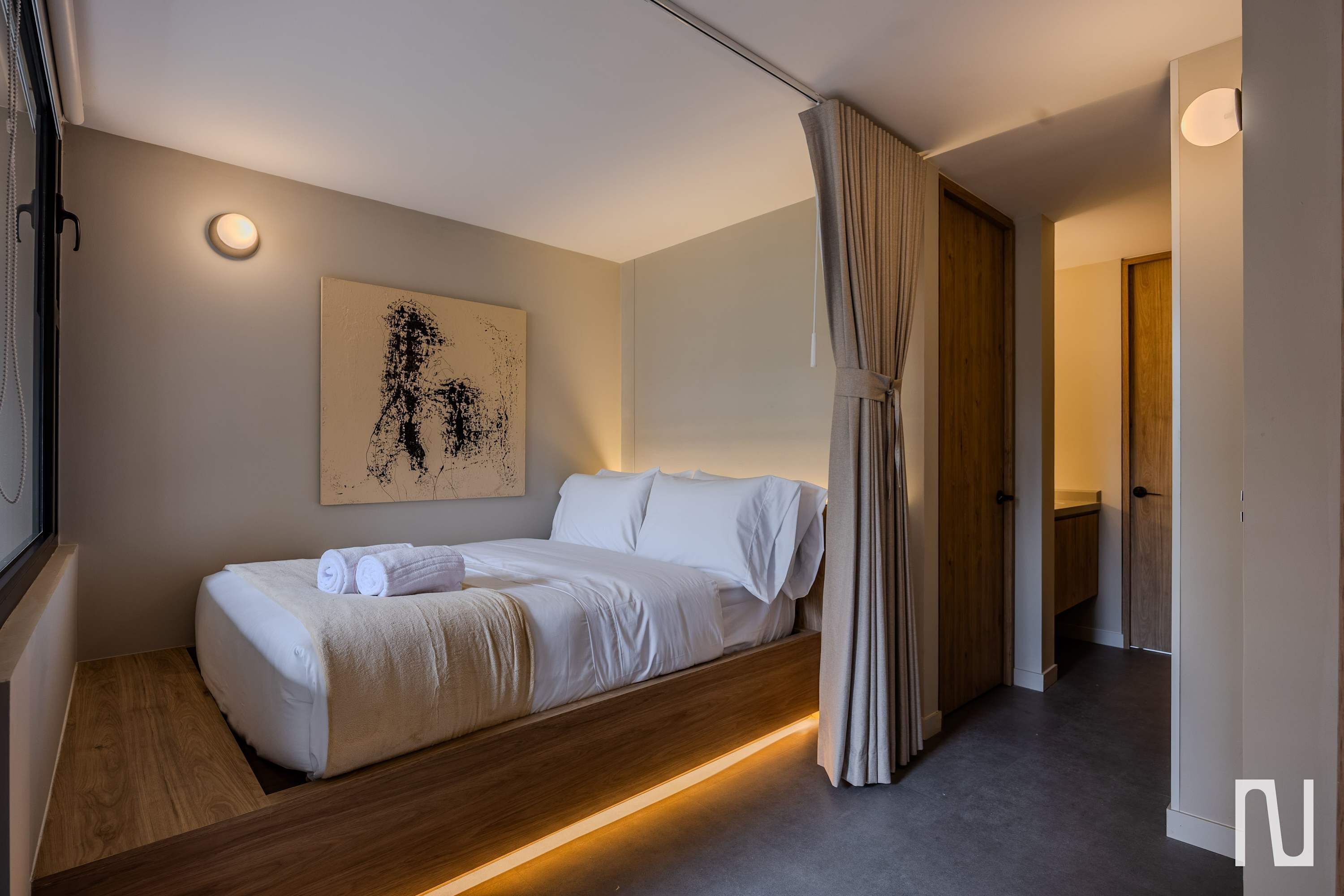 Een moderne slaapkamer met een bed, nachtkastje, wandlamp en een schilderij.