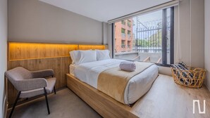 Ein modernes Hotelzimmer mit einem Holzkopfteil, einem Einzelbett mit weißen Leinen, einem grauen Sessel und einem Korbwäscheschrank.