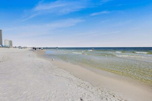 A beach with clear water, a pier, and buildings in the background. - Whimsical Way- Beach Access  Pool  built in 2025 (Gulf Shores)
