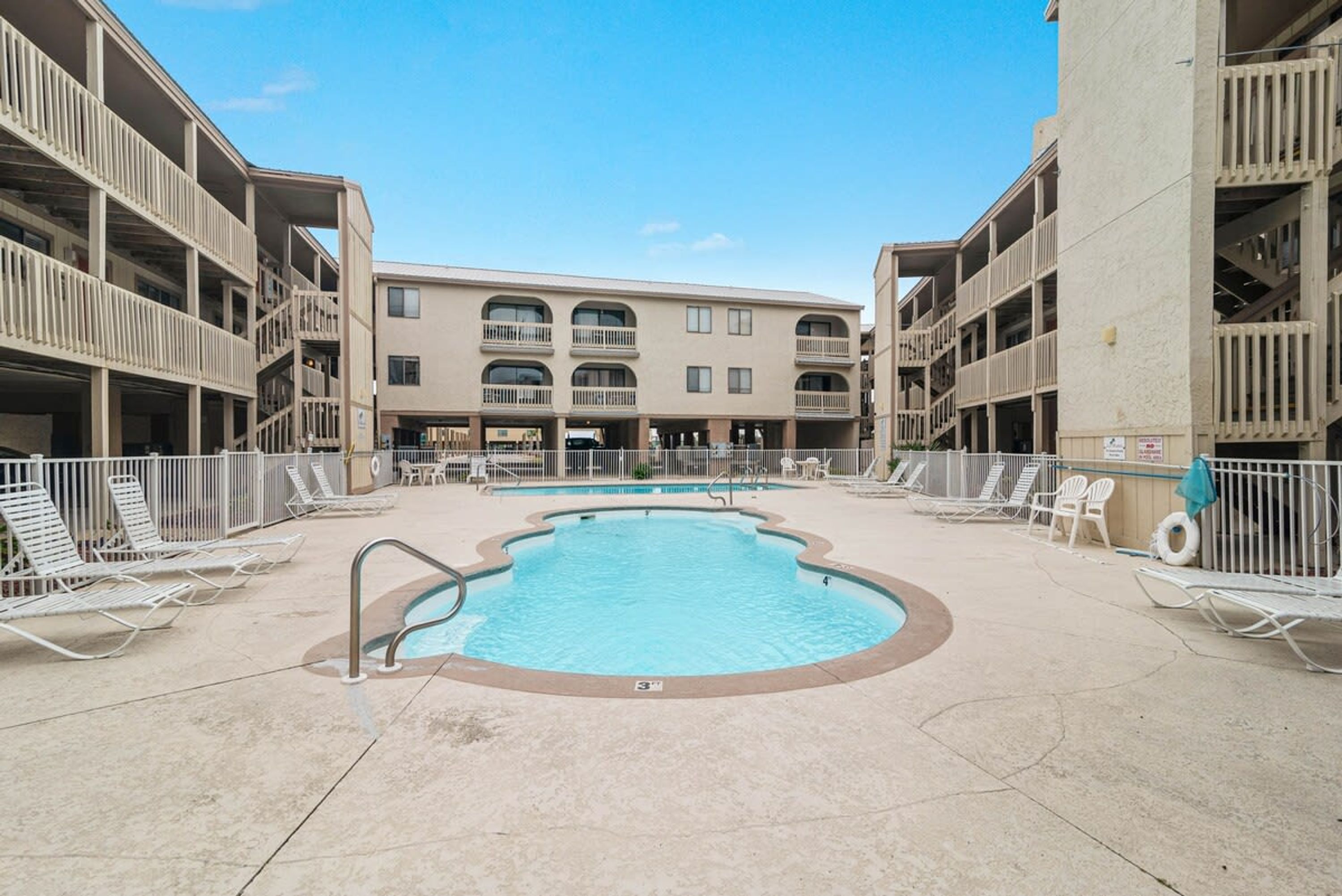 Une piscine entourée de chaises longues et un immeuble à plusieurs étages doté de balcons.