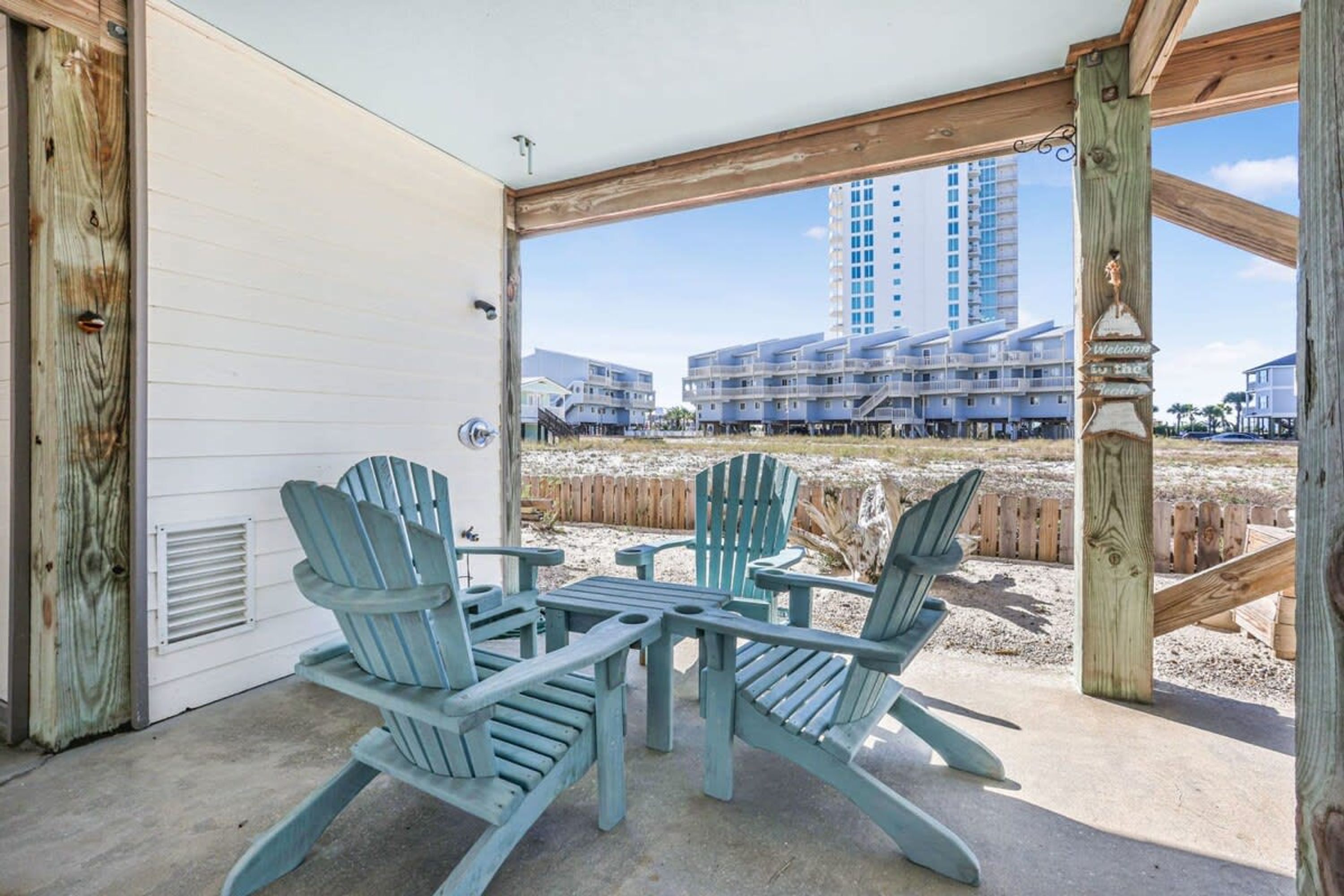 A covered patio with Adirondack chairs, a concrete floor, and a view of high-rise buildings in the background.