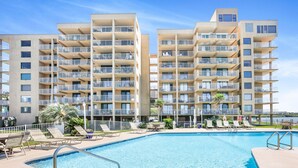 A modern hotel with a swimming pool, multiple balconies, and sun loungers. - Compass Point 201  Pet-friendly for fee  Boat ramp (Gulf Shores)