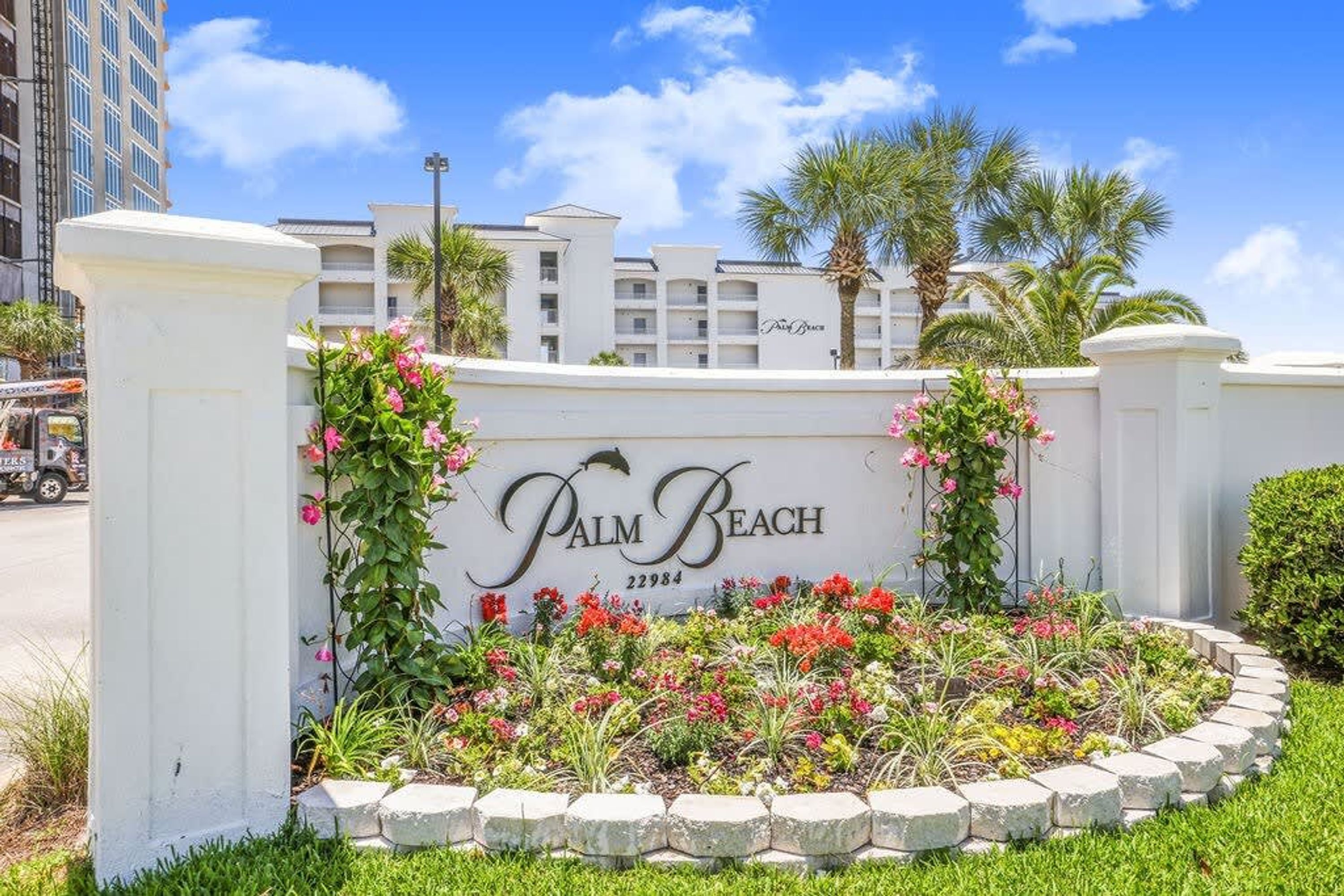 A sign for Palm Beach with a landscaped garden in front.