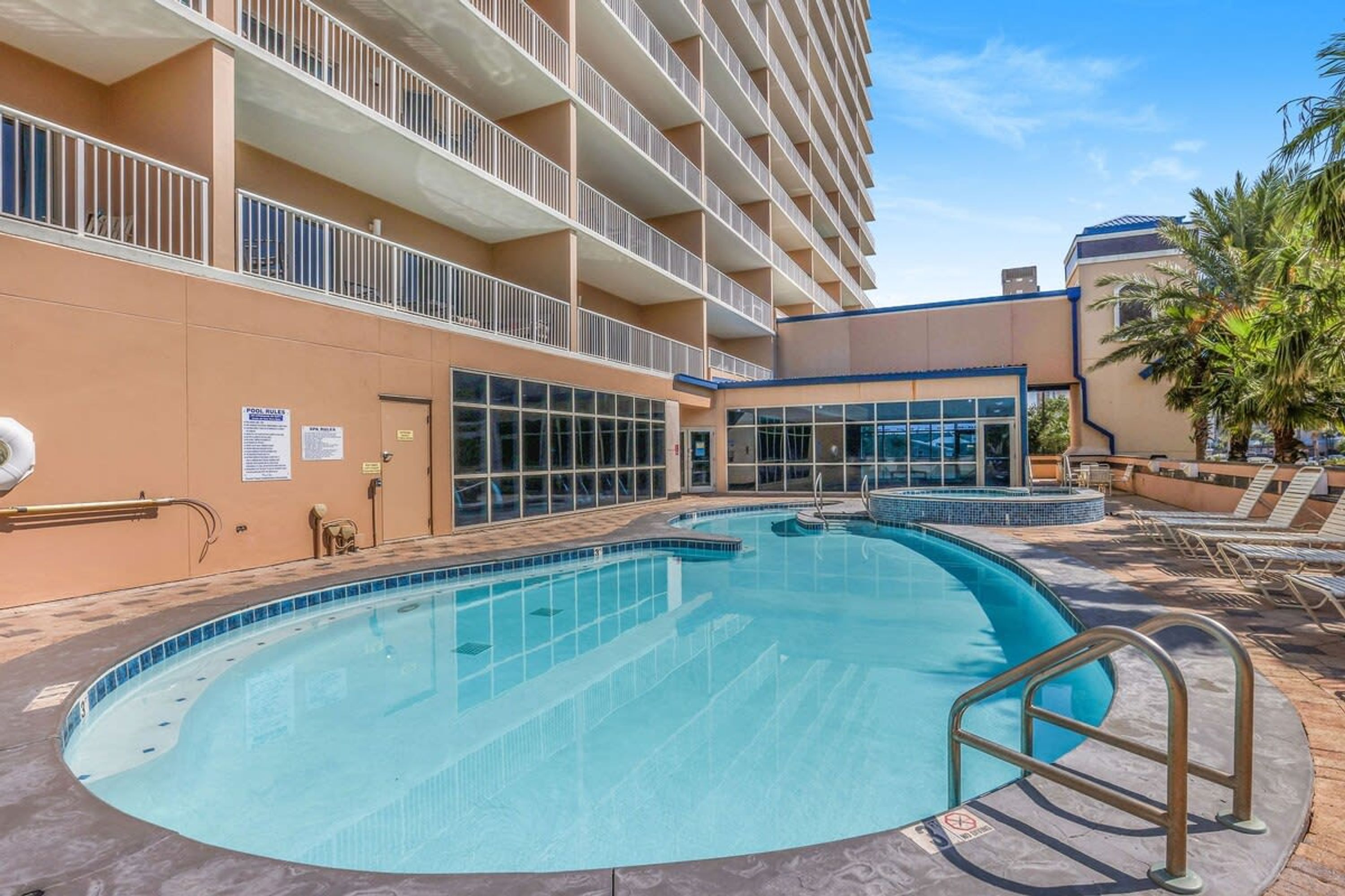 Ett hotellområde med en pool som har klart, blått vatten, en byggnad med flera balkonger och en palm som syns i bakgrunden.