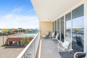 Un balcon avec vue sur la piscine, des chaises blanches et une table.