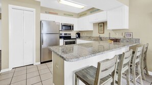 Una cocina con gabinetes blancos, electrodomésticos de acero inoxidable, encimera de granito y taburetes de bar de madera.