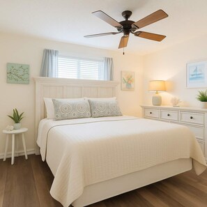 A bedroom with a bed, a nightstand, a lamp, a ceiling fan, and a window with curtains. - Lei Lani 218  Best of Beach   Bay (Orange Beach)