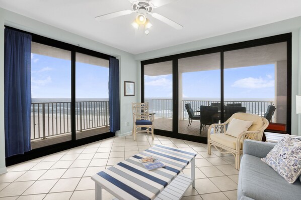 Un balcon spacieux offrant une vue sur l’océan, un coin repas avec des meubles d’extérieur et un espace détente avec un canapé et une table à rayures.