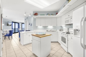 A modern kitchen with white cabinets, a central island, and a dining area with blue chairs. - Windward Pointe 801- East corner-unit  beachfront (Orange Beach)