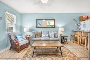A living room with a sofa, two chairs, a coffee table, and a kitchen area with a refrigerator and cabinets. - Sunrise Village 215- 2BR  1BA  gulf front  sleep 6 (Gulf Shores)
