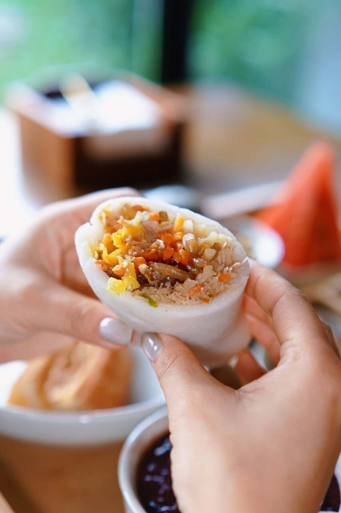 A person holding a food item with visible rice, vegetables, and possibly meat.