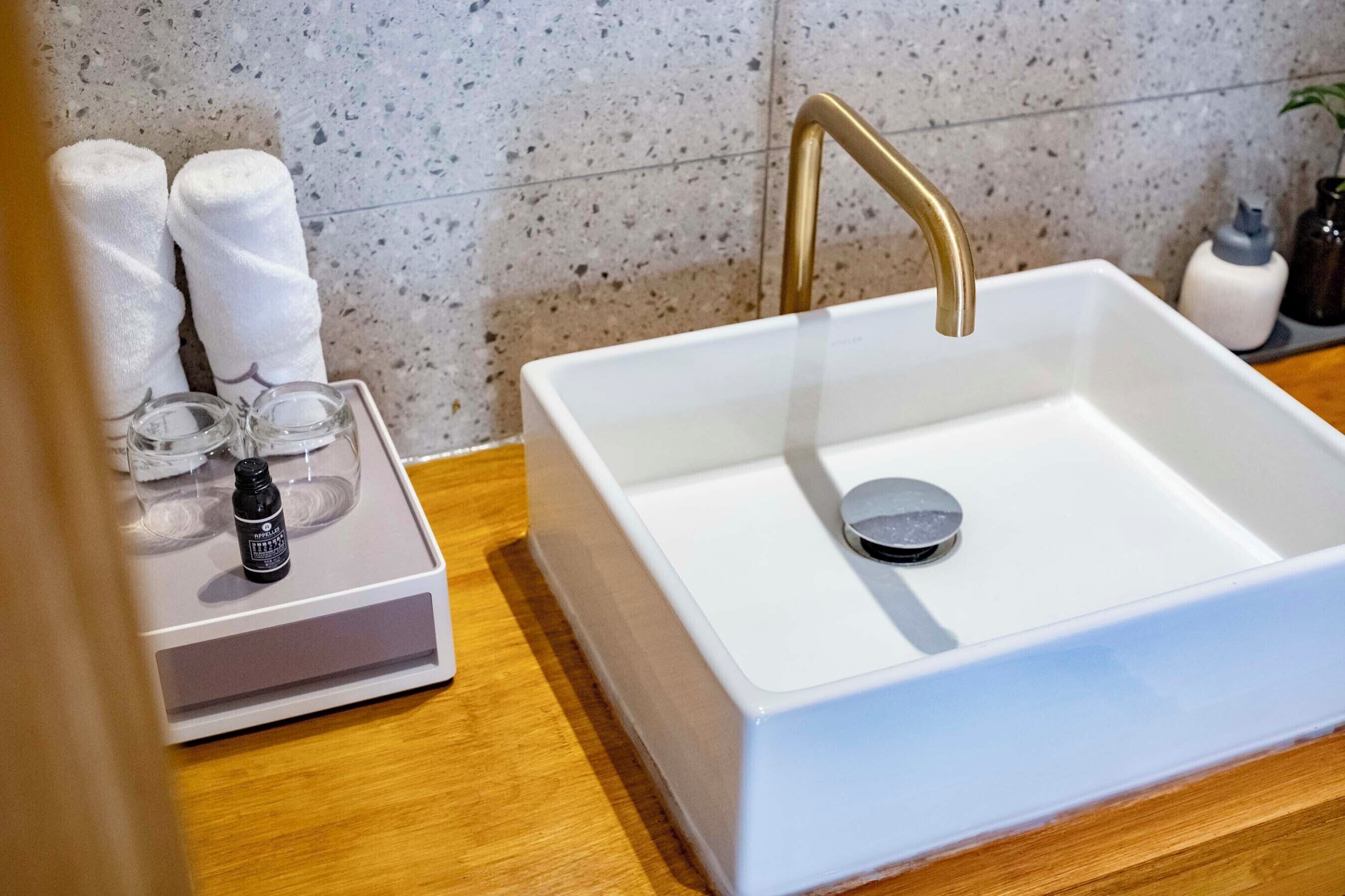 A white sink with a gold faucet, a soap dispenser, and a glass container on a wooden countertop.