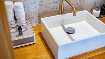 A white sink with a gold faucet, a soap dispenser, and a glass container on a wooden countertop.