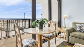 A balcony with a round table, chairs, a potted plant, a lamp, and a sofa with a view of the beach. - Island Wind West 177  Next to Hangout  pool (Gulf Shores)