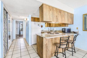 Une cuisine avec des meubles en bois, un plan de travail en granit et deux tabourets de bar.