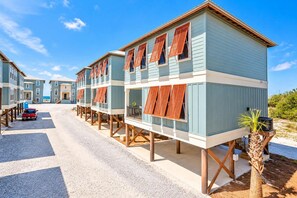 A row of beach houses with elevated platforms, each featuring a balcony and a window with shutters. - Hammock Dunes Beachside Cottage (Orange Beach)