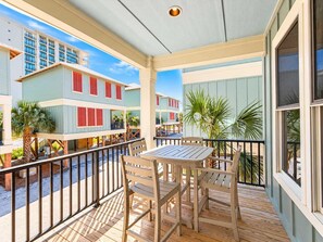 A wooden deck with a table and chairs, overlooking a street with colorful buildings. - Hammock Dunes Beachside Cottage (Orange Beach)