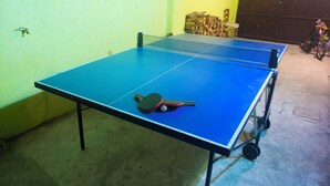 A ping pong table with a paddle, a chair, and a stack of firewood in the background. - CASA RURAL INMA (Muñoveros)