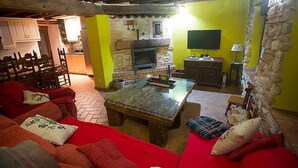 A rustic living room with a fireplace, wooden furniture, and a stone wall. - CASA RURAL INMA (Muñoveros)