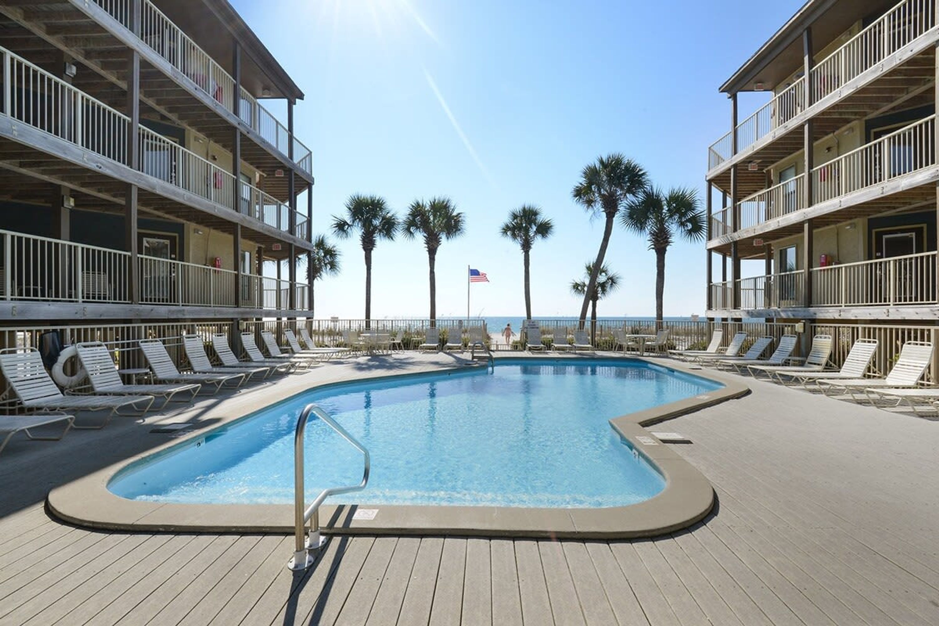 A pool area with lounge chairs and a view of the ocean.