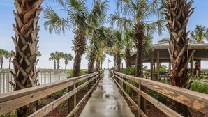 A wooden walkway flanked by palm trees leading to a covered area with benches. - Regency Isle 711  2 BR 2 5 BA  sleep 8  gulf-front (Orange Beach)