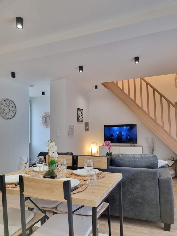 A modern living room with a dining area, a staircase, and a television.