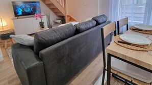 Un salon moderne comprenant un canapé, un téléviseur, un escalier et un coin repas avec des assiettes et des couverts.