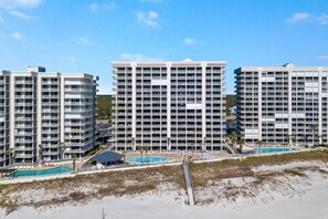 Un hotel de gran altura con múltiples balcones, una zona de piscina y vistas a la playa.