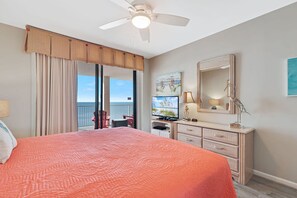 Un dormitorio con una cama grande, ventilador de techo, televisor, cómoda y vista al océano.