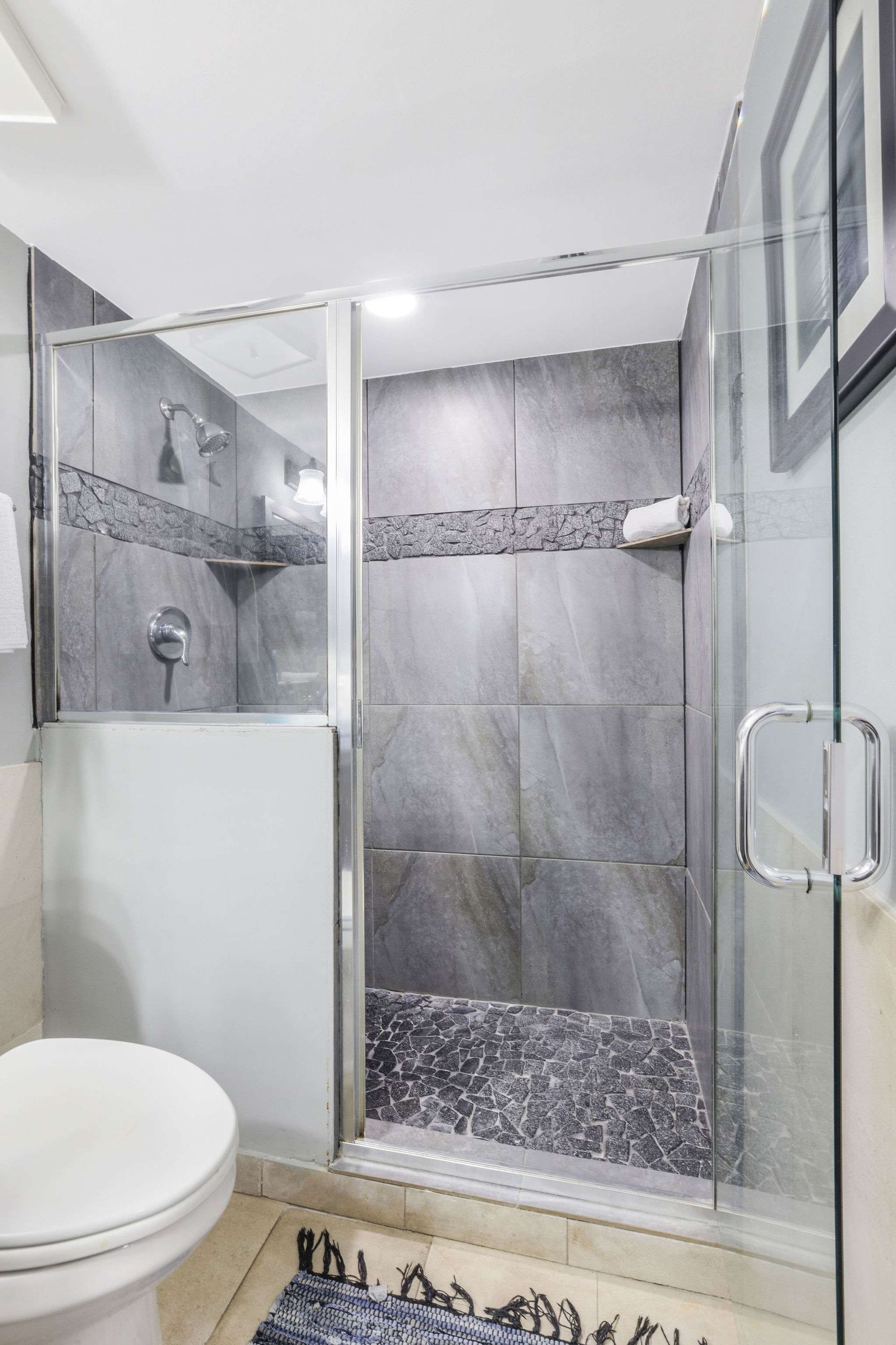 A modern bathroom with a glass-enclosed shower, a toilet, and a tiled floor.