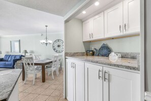 A modern kitchen with white cabinets, a granite countertop, and a dining area with a table and chairs. - Pelican Pointe1204  3BR  2BA  gulf-front (Orange Beach)
