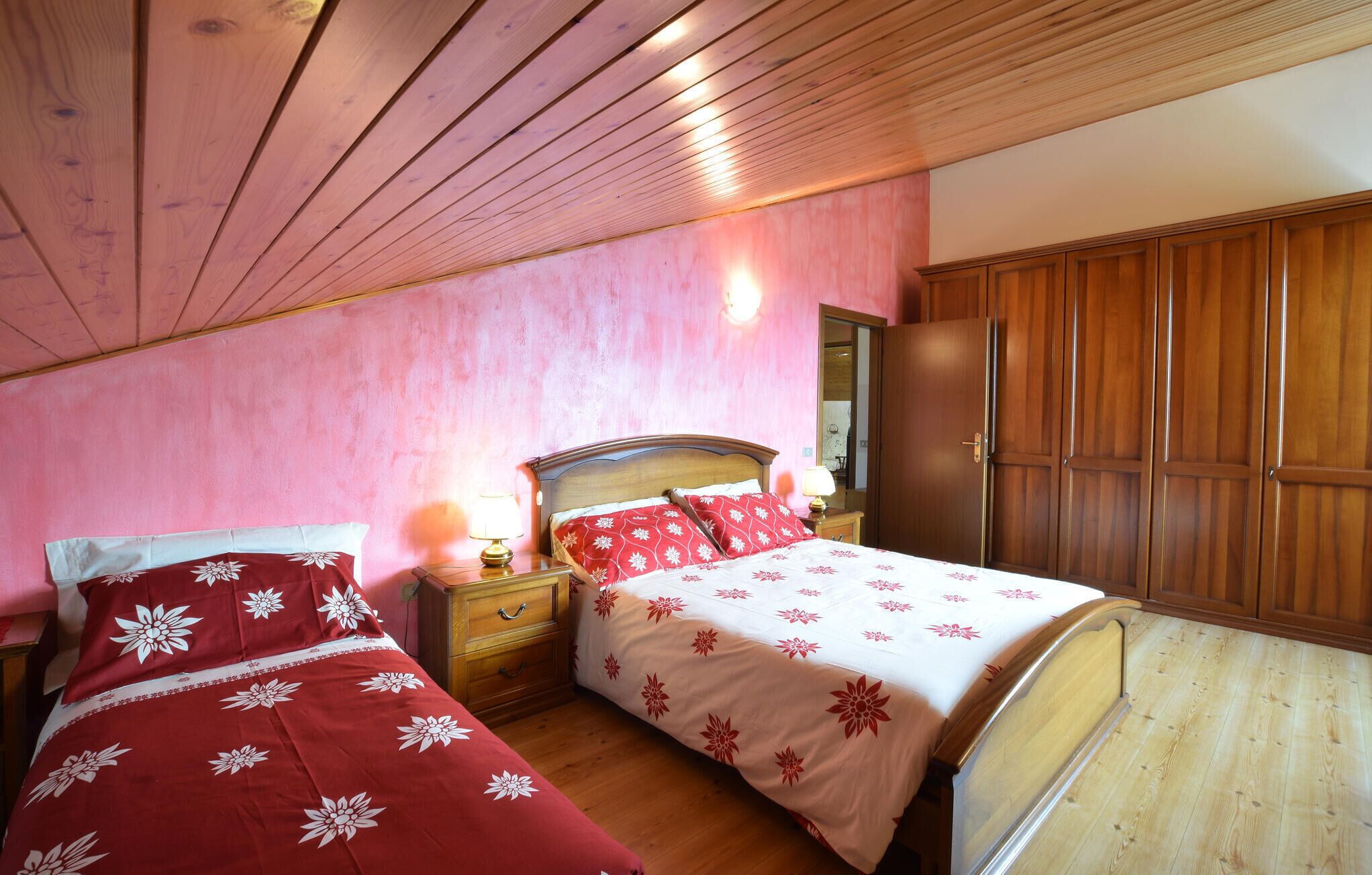 A bedroom with two beds, wooden wardrobe, and a nightstand with lamps.