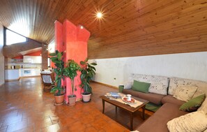 Ein geräumiger Wohnbereich mit Holzboden, einer Couch mit gemusterten Kissen, einem Couchtisch und Zimmerpflanzen.