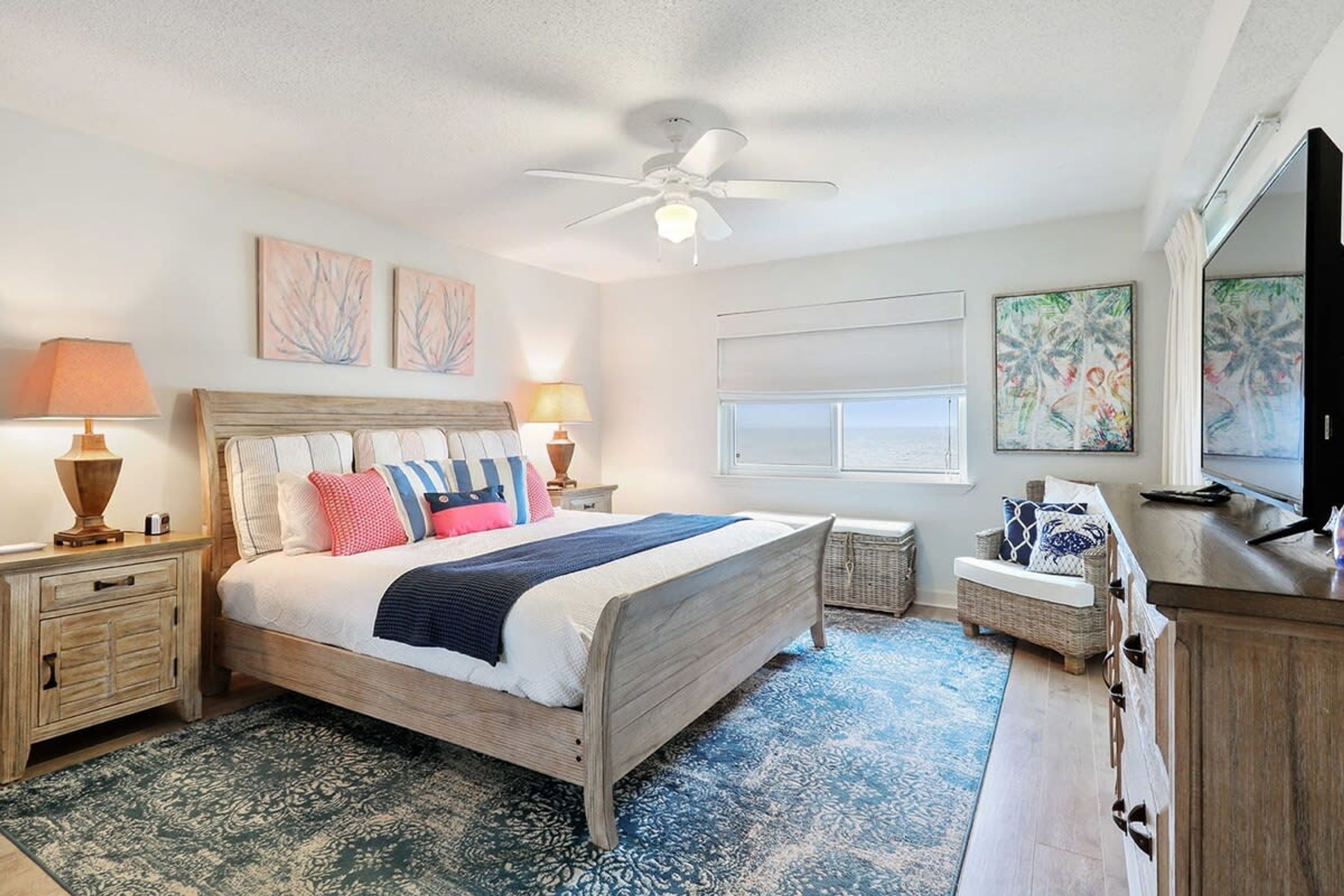 A bedroom with a wooden bed, two bedside tables with lamps, a ceiling fan, and artwork on the walls.