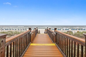 En träpromenad som leder till en strand med rader av strandstolar och parasoller.