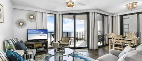 Ein geräumiges Wohnzimmer mit großem Flachbildfernseher, Deckenventilator und Balkon mit Meerblick.