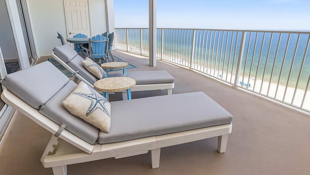 A balcony with lounge chairs and a small table, overlooking a beach. - Regency Isle  Beachfront Bliss   Amazing Views  2 bedrooms (Orange Beach)