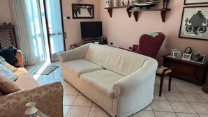 Un salon avec un canapé beige, un fauteuil à motifs, un fauteuil rouge, un téléviseur et des objets décoratifs disposés sur des étagères.